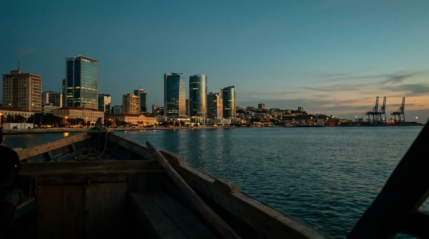 Luanda bay skyline at dusk seen from the water, glass towers along the waterfront with port cranes at the far edge